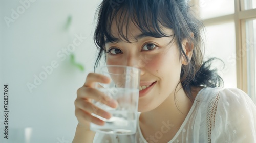 Portrait of young Asian woman holds a glass of water in her hand and smiles.