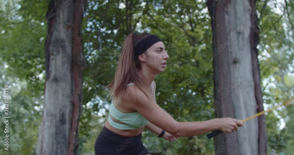Focused female badminton player practicing with racket and shuttlecock at an urban park with lush green trees in the background. Focused female badminton player practicing with racket and shuttlecock at an urban park with lush green trees in the background.