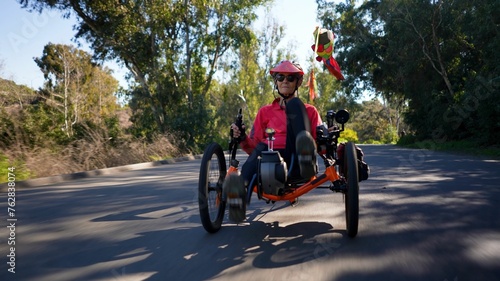 Low angle closeup of elderly senior woman riding recumbent tricycle e-bike on a path on a sunny day in a park.