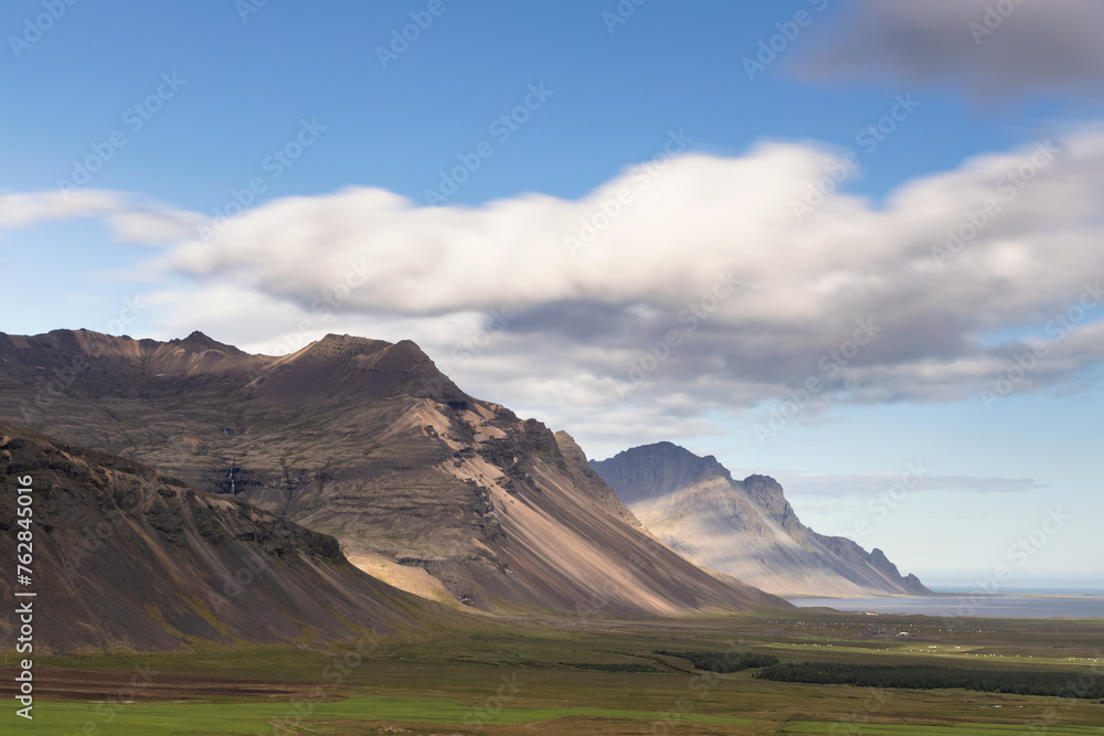 Farmlands, mountains, hills and drifting clouds at the coast of rural east Iceland.