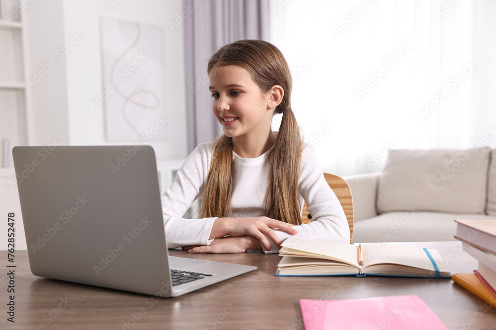 E-learning. Cute girl using laptop during online lesson at table indoors E-learning. Cute girl using laptop during online lesson at table indoors