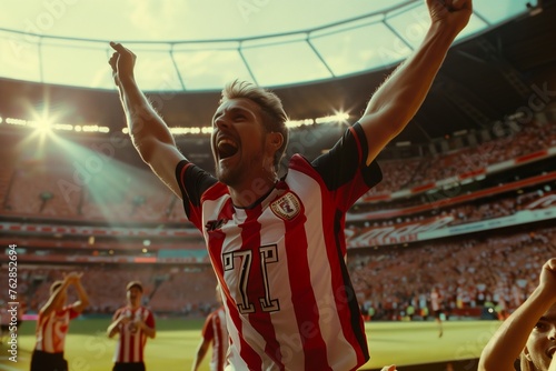 A player wearing a red and white striped sports jersey is standing on the soccer field with his arms raised in a gesture of celebration, capturing the excitement of the sports world