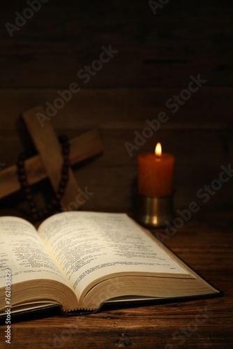Bible, cross, rosary beads and church candle on wooden table
