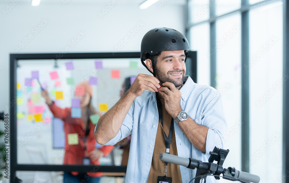 Portrait of smiling businessman riding electric scooter in office with colleague in background Portrait of smiling businessman riding electric scooter in office with colleague in background