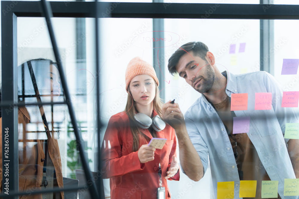 Multiethnic young business people brainstorming on a project by writing on the glass wall in the office.