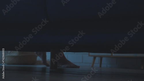 Shot of scary woman's feet walking under sofa in the darkn living room.  photo