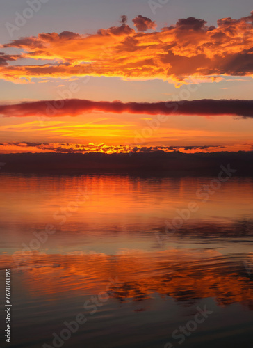 Sunset sky with reflections in water, sunlight and colored orange clouds