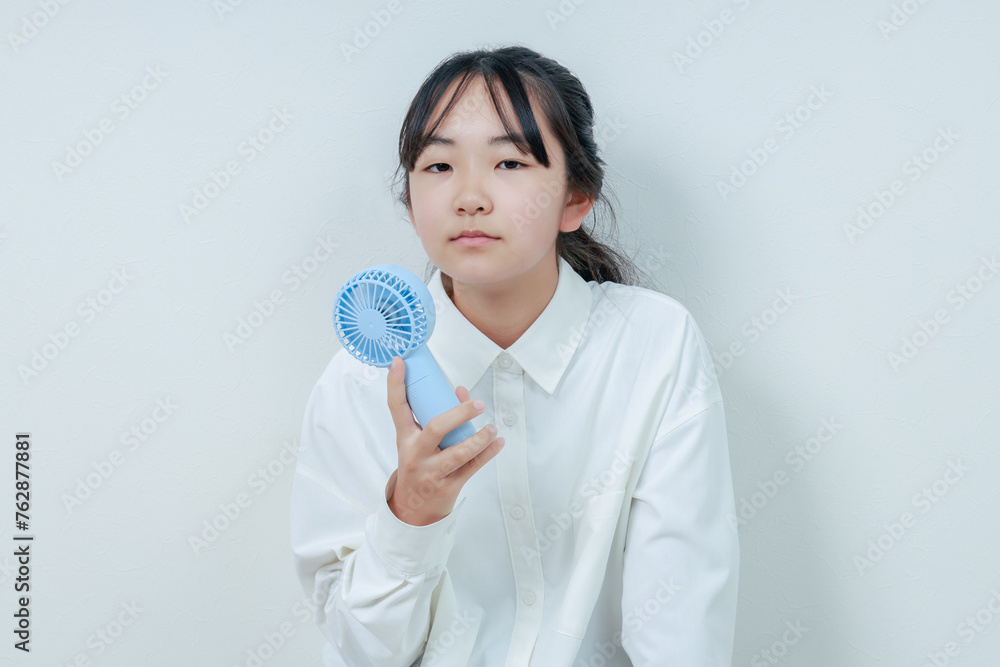 右手に扇風機を持ったカメラ目線の女の子