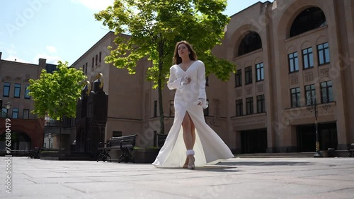 A woman in a white dress stands in front of a building