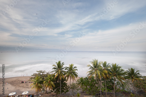 panoramic long exposure of the beach at sunrise with palm trees and waves for surfing in Palabuhanratu, Sukabumi, west Java, Indonesia photo