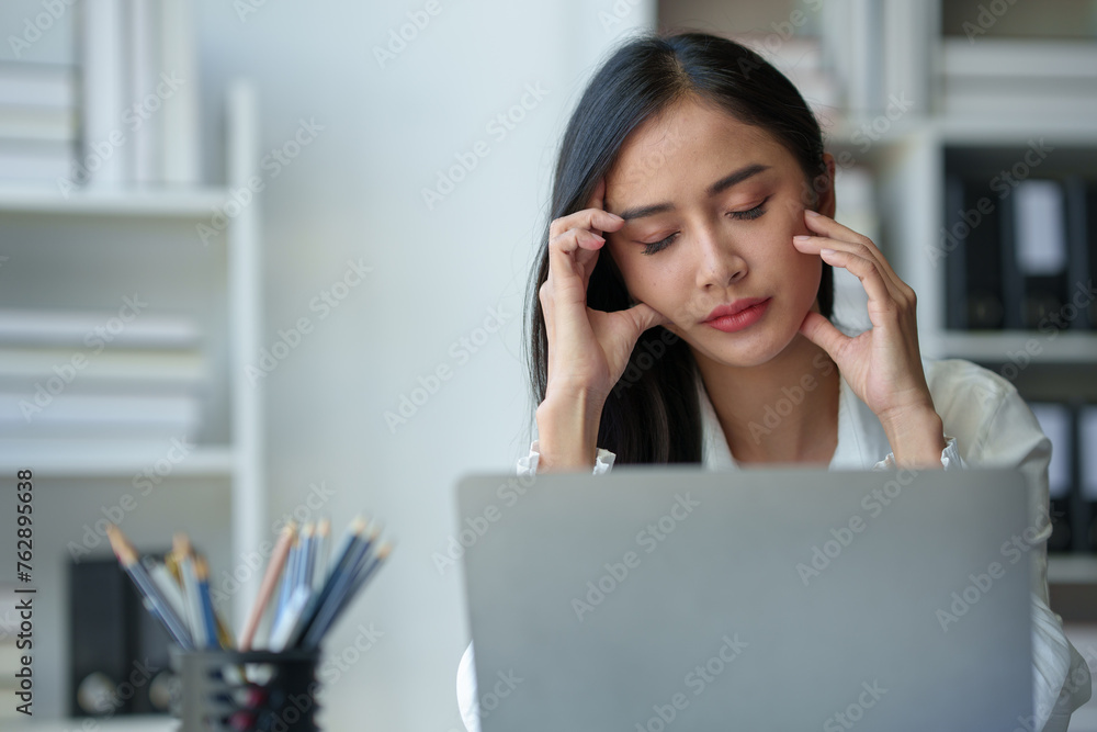 Asian businesswoman is tired, headache, sleepy and bored from sitting at a desk for a long time working on a laptop computer. Problematic financial paperwork Office syndrome concept. Asian businesswoman is tired, headache, sleepy and bored from sitting at a desk for a long time working on a laptop computer. Problematic financial paperwork Office syndrome concept.