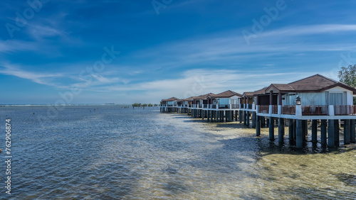 A row of water villas on stilts in the ocean. White houses with tiled roofs and terraces against the blue sky. Ripples on the clear water. Philippines. Puerto  Princesa. Palawan. photo