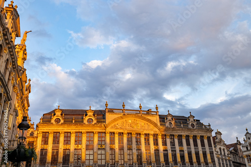 The historical guildhalls of Brussels' Grand Place bask in the warm light of the golden hour, with ornate gilded facades illuminated against a backdrop of blue skies and wispy clouds. Golden Hour Glow photo