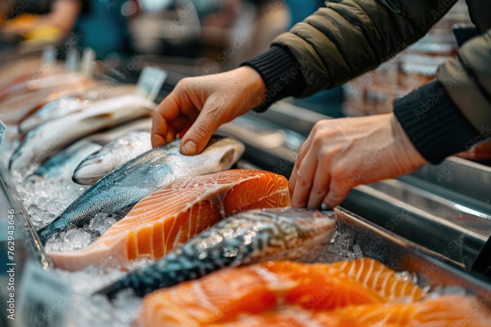 Fresh fish fillets on ice at the market. Seafood selection for a healthy diet. Variety of raw salmon, trout, and mackerel. Hand picking a piece of delicious fillet from the display.