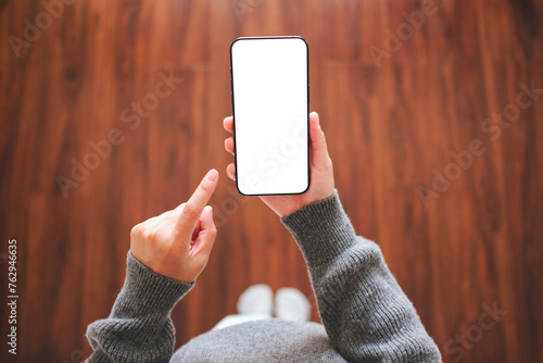 Top view mockup image of a woman holding and pointing at mobile phone with blank desktop white screen