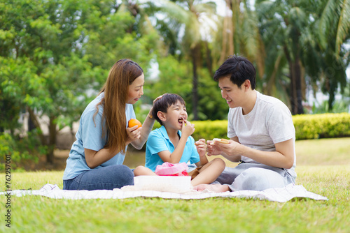 Happy cheerful Asian family with father, mother, and little son enjoy picnic together in a weekend at a park.