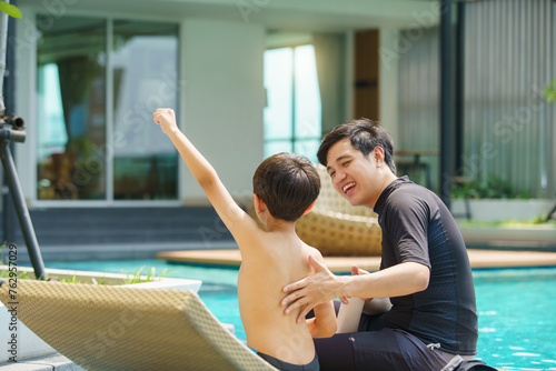 Father is applying a sun screen or sun block lotion on his son body before going to swimming in the swimming pool.  photo