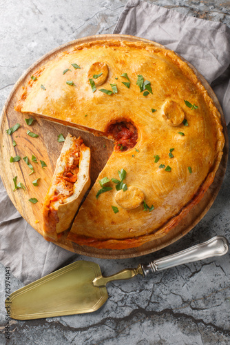 Empanada gallega is a traditional savory pie from the Spanish filling is with meat, bell pepper, tomato and onion closeup on the board on the table. Vertical top view from above