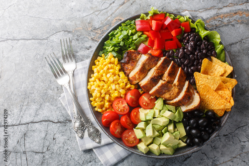 Southwest salad of chicken, corn, peppers, olives, avocado, tomatoes and onions close-up on a board on the table. Horizontal top view from above