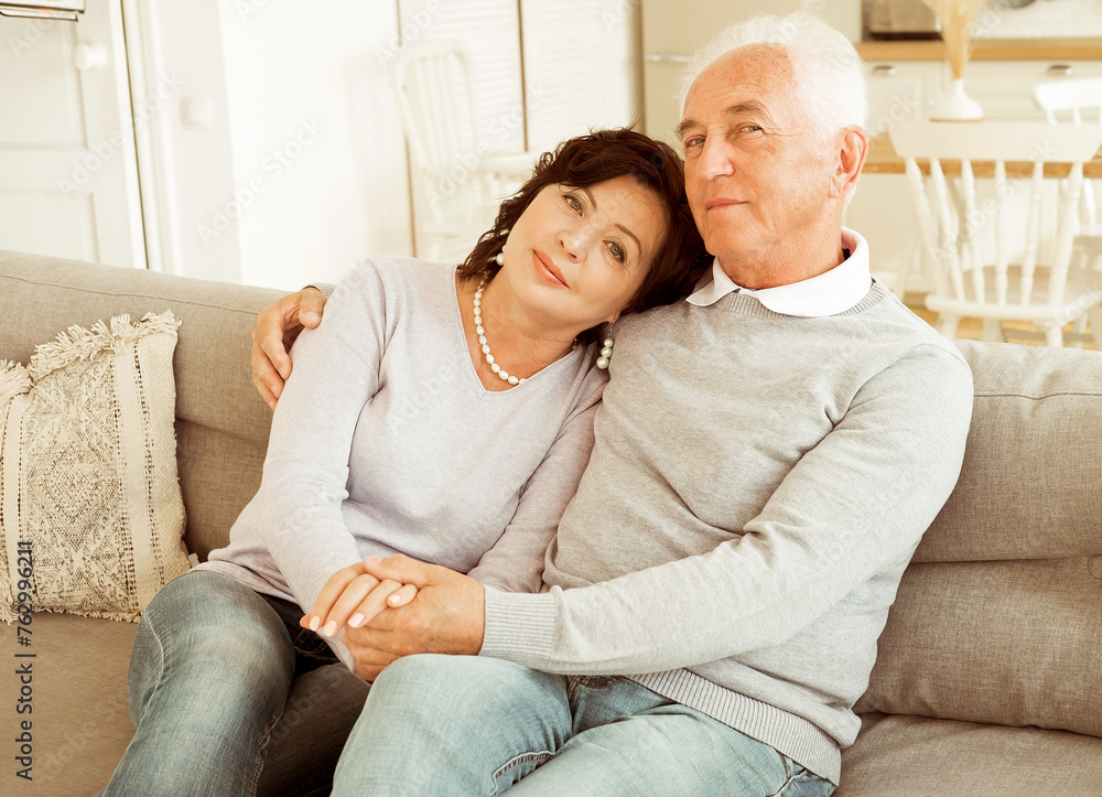 An elderly couple hugging while sitting on the floor of the living room. Relationship and family concept.
