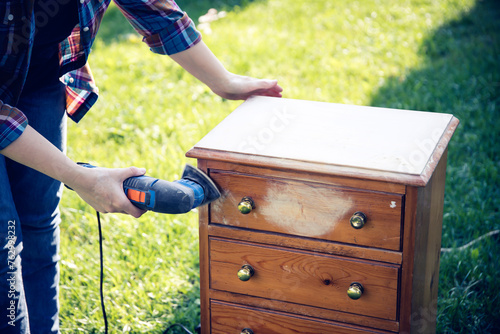 Person using a grinder removes old paint from furniture, restoration of antique furniture
