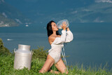 Sexy woman in lingerie drink milk from can and bottle against countryside. Sexy woman drinking milk in Alps. Sensual woman eat milk near Swiss Alps. Beautiful woman enjoys milk on alpine village.