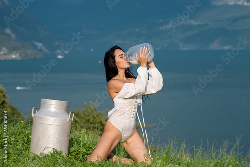 Sexy woman in lingerie drink milk from can and bottle against countryside. Sexy woman drinking milk in Alps. Sensual woman eat milk near Swiss Alps. Beautiful woman enjoys milk on alpine village.