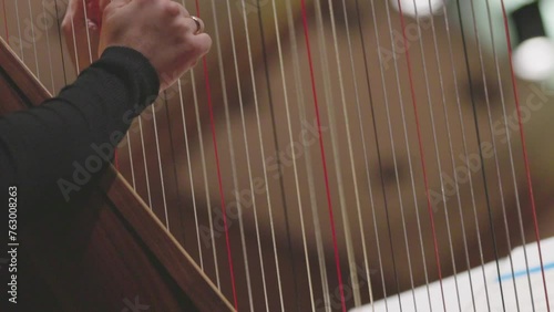 A slow motion video of a musician playing the harp by plucking the strings of the instrument during a classical symphony orchestra performance. Nr. 2
