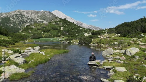 Woman sits on Rock at Water River in Pirin Mountains National Park, Bulgaria photo
