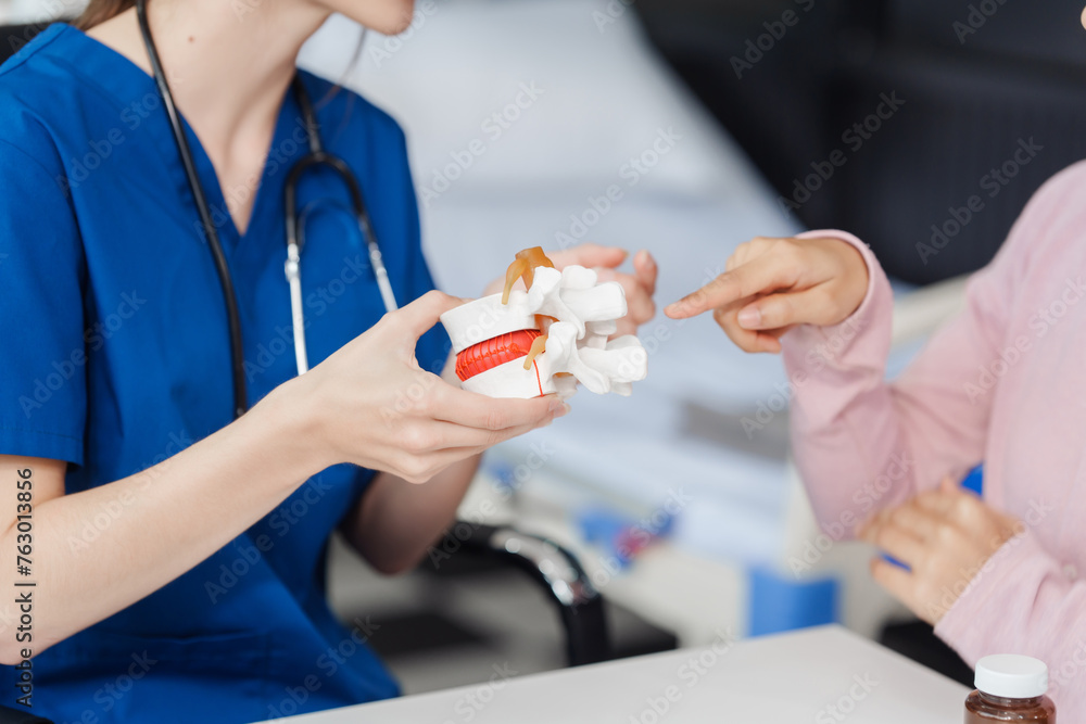 Caucasian female doctor explain to asian female patient using Human Anatomical Lumbar Disc Herniation Model at desk in medical room, medical learn aid anatomy instrume - obrazy, fototapety, plakaty 