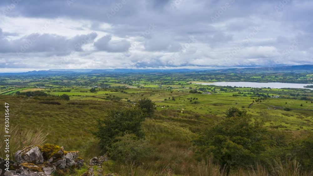 Timelapse of rural nature farmland with rocks, trees and sheep in the foreground field and hills and lake in distance during sunny cloudy day viewed from Carrowkeel in county Sligo in Ireland. Timelapse of rural nature farmland with rocks, trees and sheep in the foreground field and hills and lake in distance during sunny cloudy day viewed from Carrowkeel in county Sligo in Ireland.