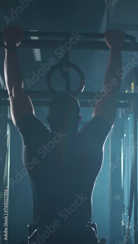 Athlete in wheelchair performs pull-ups on the horizontal bar, gym training and physical activity, vertical video, people with disabilities.