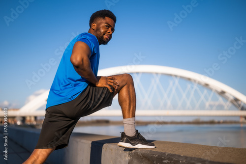 Young african-american man is exercising in the city. He is stretching his body.