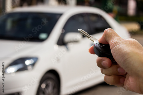 Female hand holding car key ready to start a new car with blurred car background.hand hold key blur car parking.