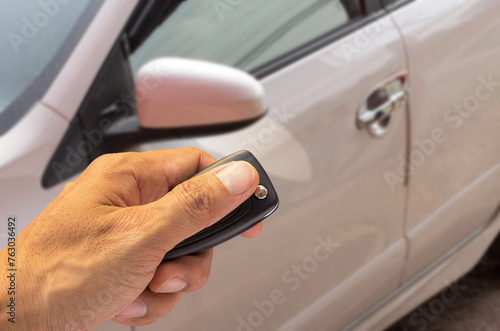 Man hand holding car key ready to start a new car with blurred car background.hand hold key blur car parking.
