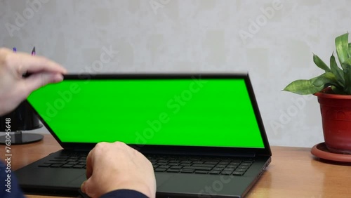 The user closes the laptop lid after finishing working with a green screen chromakey mockup. Remote work concept.