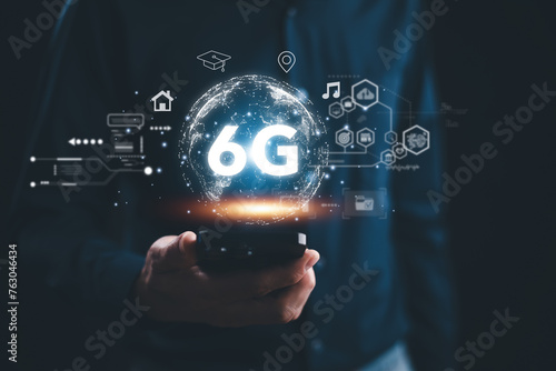 A person is holding a cell phone with the word 6G on it. The image is a representation of the future of technology and the advancements that will be made in the field of telecommunications