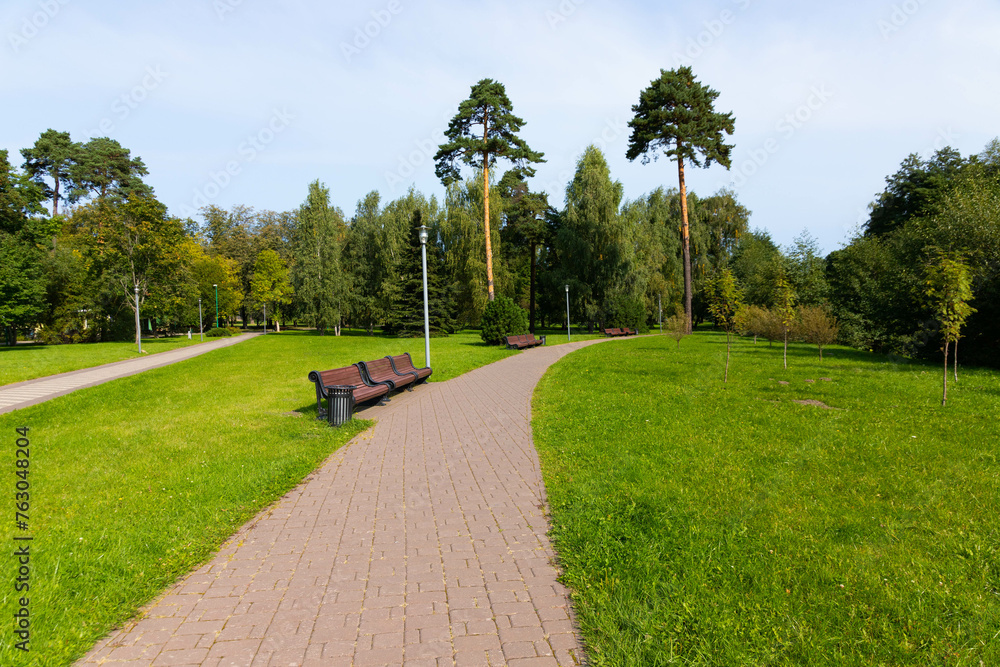 Park path with benches, green grass and trees.