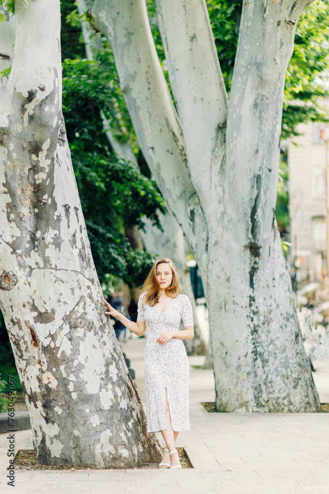 A cute girl walks in the park in a light dress. a charming blonde is resting in nature A cute girl walks in the park in a light dress. a charming blonde is resting in nature