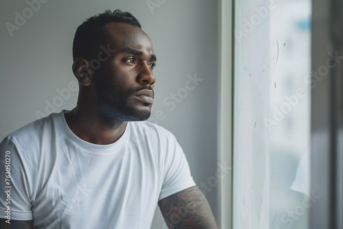 depressed african american man in white t-shirt with tattoo on arms looking through window © JAYDESIGNZ