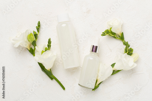 Facial cosmetic products with freesia flowers on concrete background  top view