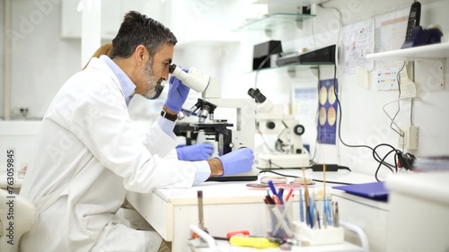 Scientist using a microscope in a clinical lab with equipment around