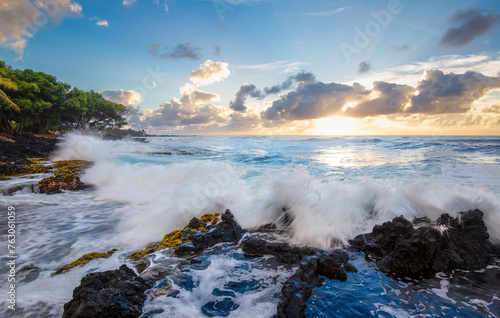 Sunset over the sea, waves crashing on the rocks, palm trees on the beach in Hawaii. Big Island, United States of America.
