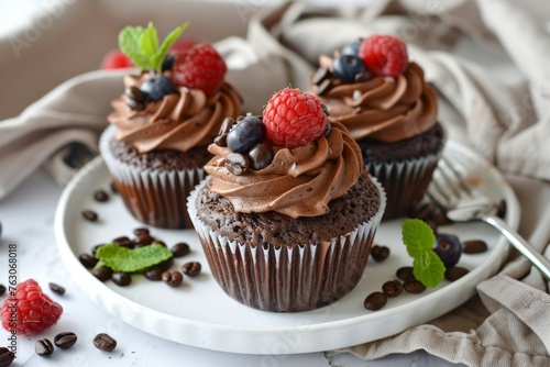 Home-baked chocolate cupcakes with fresh berries and chocolate covered espresso beans on a white background with plate and fork.