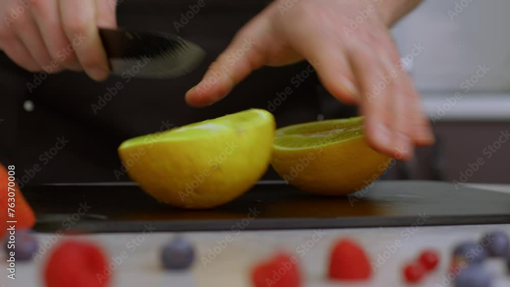 A close-up shows drops of water on a bright orange. The cook skillfully cuts an orange into slices with a kitchen knife. In the slow-motion video, splashes of orange juice are clearly visible. A close-up shows drops of water on a bright orange. The cook skillfully cuts an orange into slices with a kitchen knife. In the slow-motion video, splashes of orange juice are clearly visible.