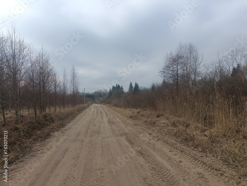 Road in forest in Siauliai county during cloudy early spring day. Oak and birch tree woodland. cloudy day with white clouds in blue sky. Bushes are growing in woods. Sandy road. Nature. Miskas. 