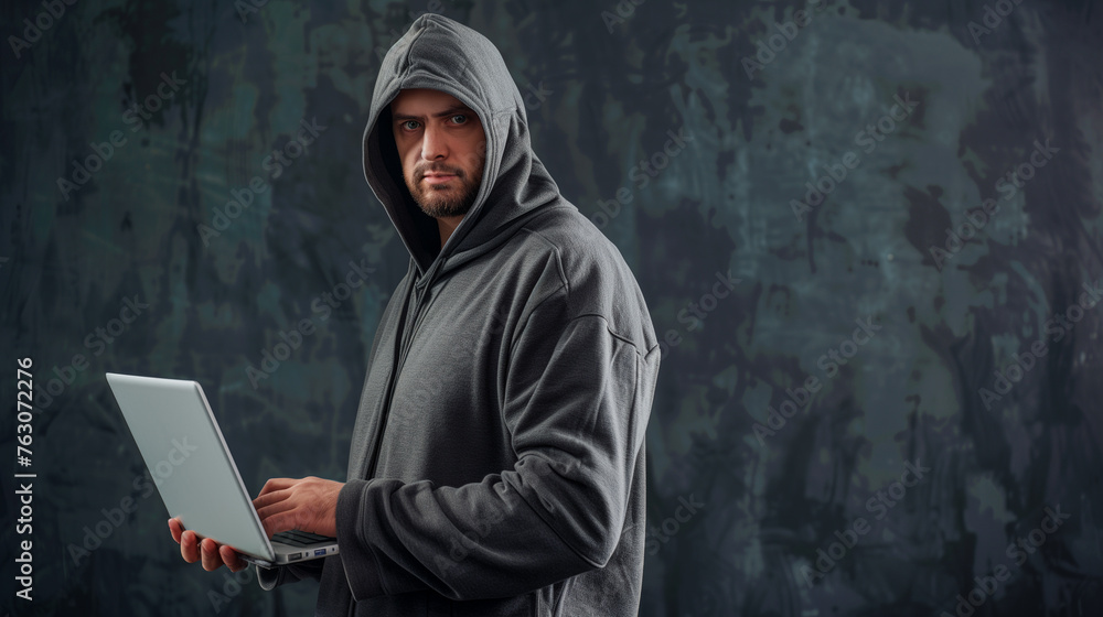 Hacker man with hoodie suit holding a laptop computer on dark black background Hacker man with hoodie suit holding a laptop computer on dark black background