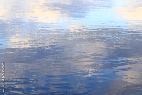 Reflection of clouds in water. The surface of water in a lake, river or flooded quarry. Ripples on the water. Beautiful color of water. Natural background