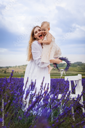 A happy mother hugs her daughter and smiles while standing near a white chair in a lavender field