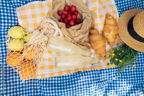 A small picnic with croissants, strawberries, and lemonade on a blue checkered blanket